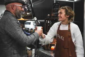 Nobel Coffee's barista som serverer en café latte brygget i vores kaffevogn til en glad kunde 